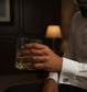 Luxury tuxedo shirt studs showcased on a gentleman's cuff while holding a drink in an elegant setting.